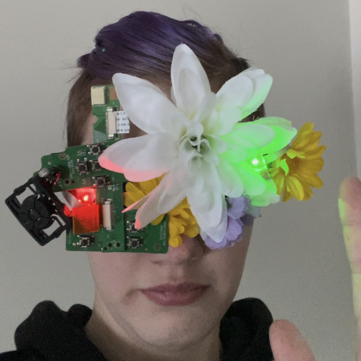 me wearing my mask, it has circuitboards and a button on the left with a red light and flowers on the right with a green light. both lights are lit,